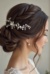 The image shows a woman wearing a white dress and a beautiful bridal hair comb adorned with pearls and crystals. The background is blurred, giving the image a dreamy and romantic feel.