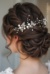 The image shows a woman wearing a white dress and a beautiful bridal hair comb adorned with pearls and crystals. The background is blurred, and there is a watermark on the image.