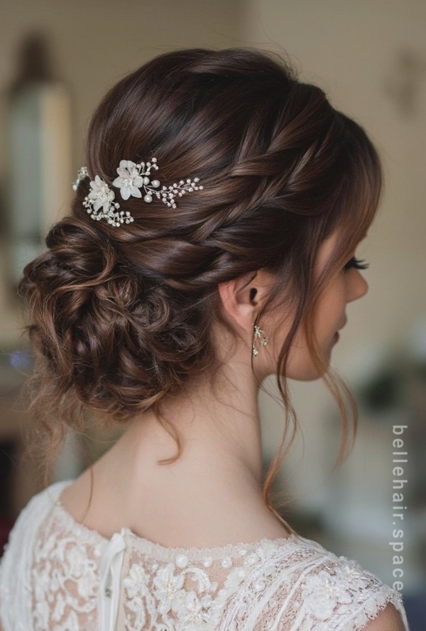 The image shows a woman wearing a white dress with a beautiful wedding hairstyle featuring a flower in her hair. The background is blurred, and there is a watermark on the image.